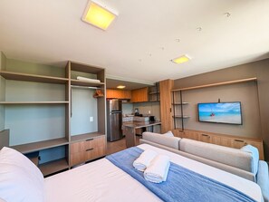 A hotel room with a bed, a seating area, a kitchenette, and a TV on the wall. - Portal dos Mares - Beira-Mar Tamandaré (Tamandaré)
