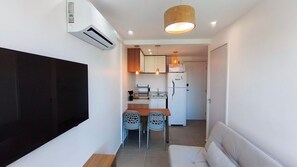 A compact living space with a kitchenette, a dining area with two chairs, a sofa, and an air conditioning unit mounted on the wall. - Portal dos Mares - Beira-Mar Tamandaré (Tamandaré)