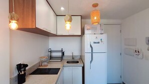 A compact kitchen with a white refrigerator, a microwave, a sink, and pendant lighting. - Portal dos Mares - Beira-Mar Tamandaré (Tamandaré)