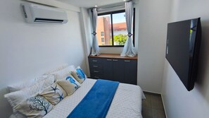 A bedroom with a bed, a dresser, a TV, and a window with curtains. - Portal dos Mares - Beira-Mar Tamandaré (Tamandaré)