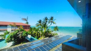 Blick auf einen Strand mit Solaranlagen, Palmen und einem Gebäude mit rotem Dach.
