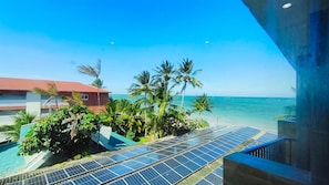 A view of a beach with solar panels, palm trees, and a building with a red roof. - Portal dos Mares - Beira-Mar Tamandaré (Tamandaré)