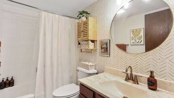 A bathroom with a white toilet, a bathtub, a sink with a mirror, and a shower curtain.
