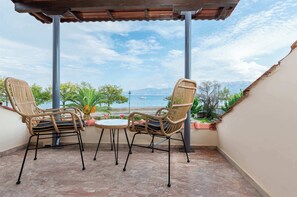 Un balcón techado con dos sillones de mimbre y una pequeña mesa, con vistas a un cuerpo de agua y montañas.