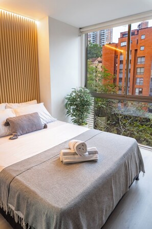 Une chambre d’hôtel moderne avec un grand lit, une vue sur la ville et un balcon agrémenté d’une plante.