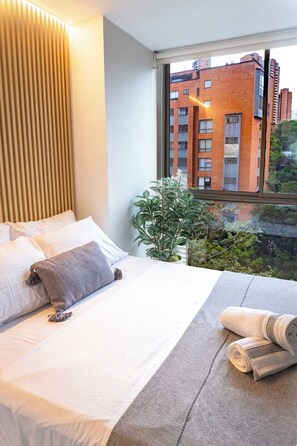 Ein Hotelzimmer mit Bett, Fenster mit Blick auf Gebäude und einer Pflanze.
