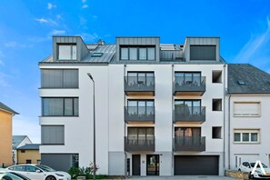 Un immeuble résidentiel à plusieurs étages, doté de balcons, d’un garage et donnant sur la rue.