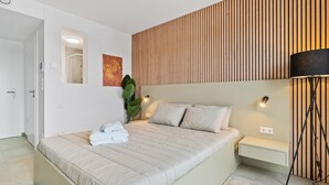 A modern bedroom with a large bed, bedside tables, a lamp, and a wooden panel wall. - Stylish Coliving Rooms for Work, Rest, and Play (Luxembourg)