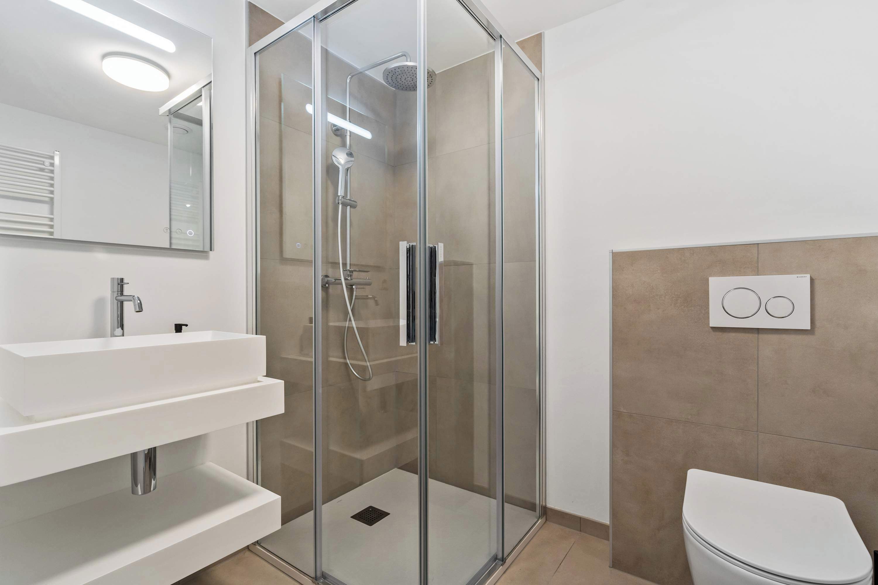 A modern bathroom with a glass-enclosed shower, a white sink with a mirror, and a toilet.