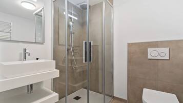 A modern bathroom with a glass-enclosed shower, a white sink with a mirror, and a toilet.