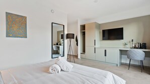 Ein modernes Hotelzimmer mit einem großen Bett, einem Schreibtisch, einem Sessel, einem Flachbildfernseher und einem Kleiderschrank.