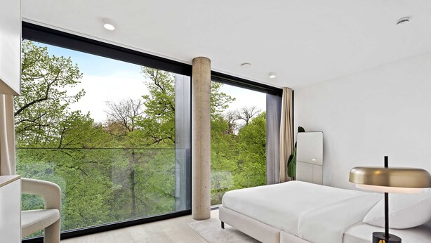 Um quarto moderno com uma janela grande, uma cama, uma mesa de cabeceira e uma cadeira.
