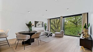Uma sala de estar moderna com área de refeições, janelas grandes e vista para o verde.