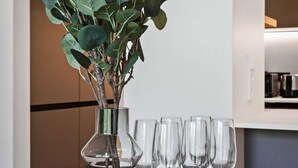 Uma mesa de jantar com um vaso de folhagem verde e seis copos de vinho.