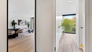 Interior moderno com área de jantar, sofá e vista para o verde através de uma grande janela.