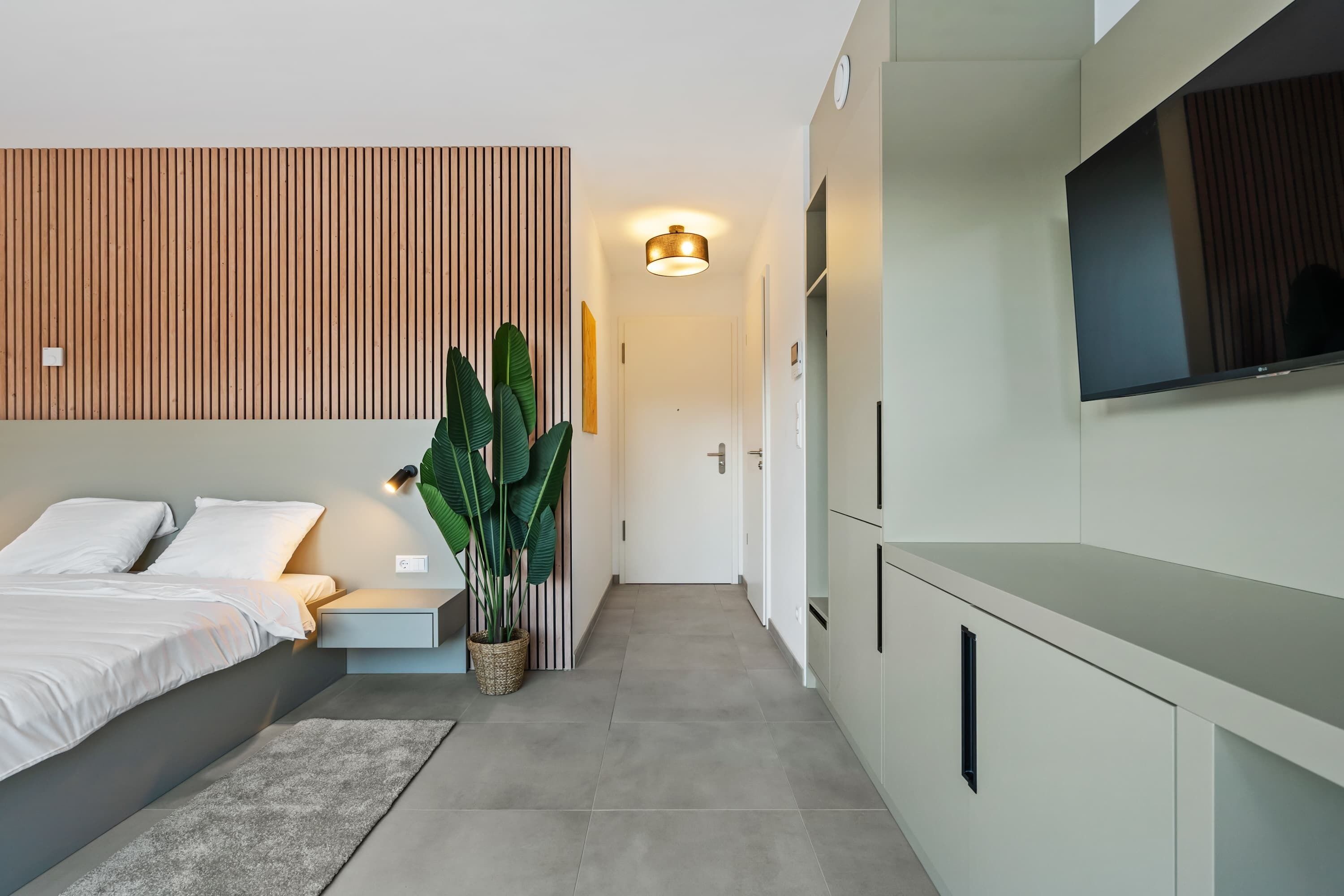 Een moderne slaapkamer met een bed, nachtkastje en een grote kamerplant.