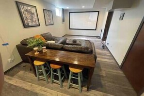 Ein modernes Wohnzimmer mit einer Eckcouch, einem Holzesstisch mit Hockern und einem an der Wand montierten Flachbildfernseher.