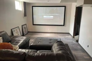 Una sala de estar con un televisor de pantalla plana grande montado en la pared, un sofá de cuero y una mesita de centro pequeña.