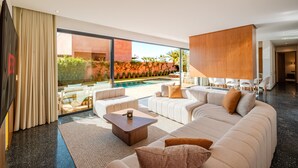 Un salon moderne avec un grand canapé d’angle, une table basse et une vue sur une piscine et un espace de détente extérieur.