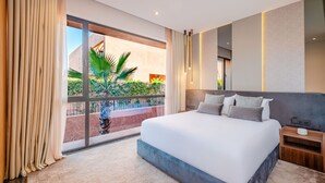 Une chambre d’hôtel moderne avec un grand lit, une table de chevet et une vue sur un balcon agrémenté de plantes.