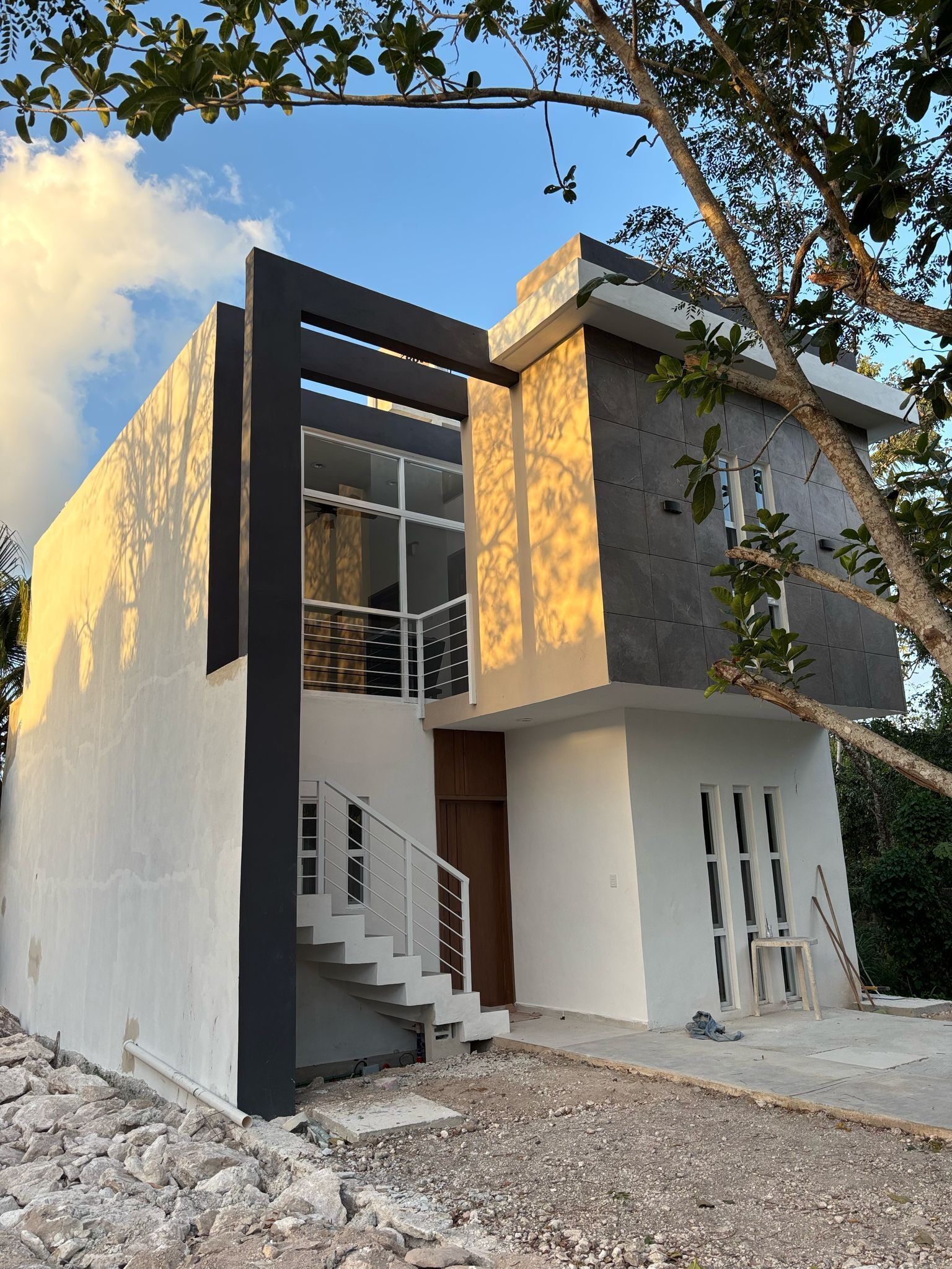 A modern two-story house with a balcony, a staircase, and a view of the surrounding trees.