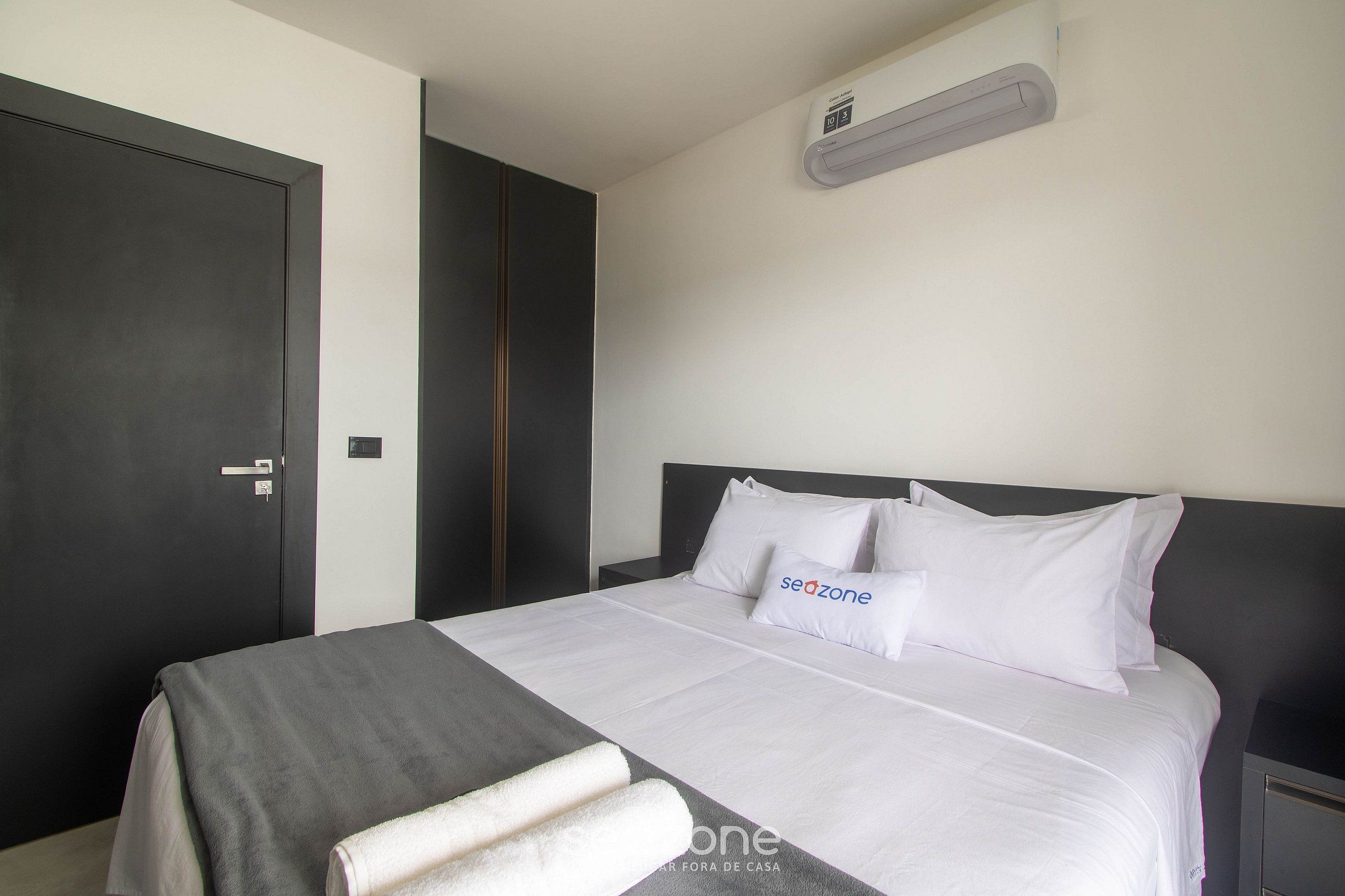 A modern hotel room with a large bed, a dark wardrobe, and a wall-mounted air conditioner.