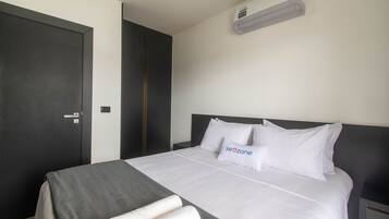 A modern hotel room with a large bed, a dark wardrobe, and a wall-mounted air conditioner.
