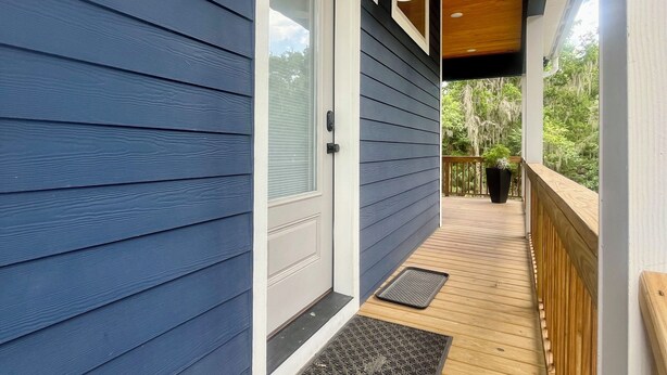 Eine überdachte Veranda mit Holzterrasse, einer weißen Tür und einem kleinen Blumentopf.