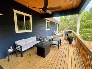 Une terrasse couverte avec un canapé, des chaises, une table et un barbecue.