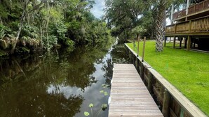 Eine hölzerne Stegfläche, die sich in ruhiges Wasser erstreckt, umgeben von üppiger Vegetation und Bäumen.