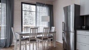 Et moderne køkken med et rustfrit stål køleskab, et spisebord med stole og et vindue med gardiner.