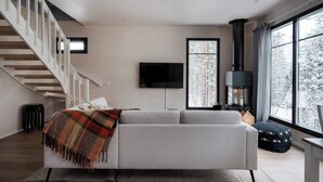 En moderne stue med en hvid sofa, et ternet tæppe, en pejs, et fjernsyn og en trappe.