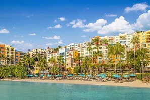 Ein Hotel am Strand mit mehreren bunten Gebäuden, Palmen und Strandsonnenschirmen.