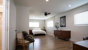 A spacious bedroom with a bed, a chair, a dresser, and a ceiling fan. - The Atlas House | Stay, Surf, and Spin | San Diego (San Diego)