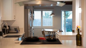A modern kitchen with a central island, a dining table, and a view of the outdoors through a window. - The Atlas House | Stay, Surf, and Spin | San Diego (San Diego)