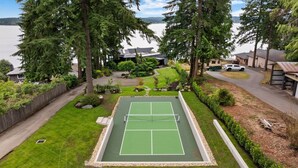 Cancha de tenis rodeada por un patio cercado, con vista a un lago y edificios residenciales.