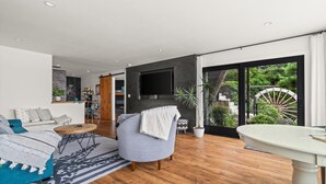 Una sala de estar moderna con un sofá, una mesa redonda de centro, un televisor montado en la pared y un ventanal con vistas a zonas verdes.