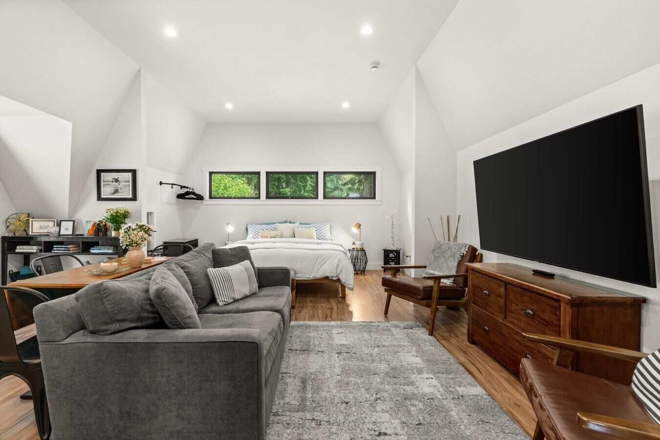 A modern bedroom with a large bed, a desk, a sofa, and a TV.