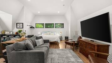 A modern bedroom with a large bed, a desk, a sofa, and a TV.