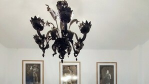 Een woonkamer met een donkergrijze bank, zes ingelijste foto's aan de muur en een zwarte kroonluchter.