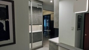Een moderne badkamer met een grote spiegel, een kunstwerk in een lijst aan de muur, en een glazen deur naar een andere ruimte.
