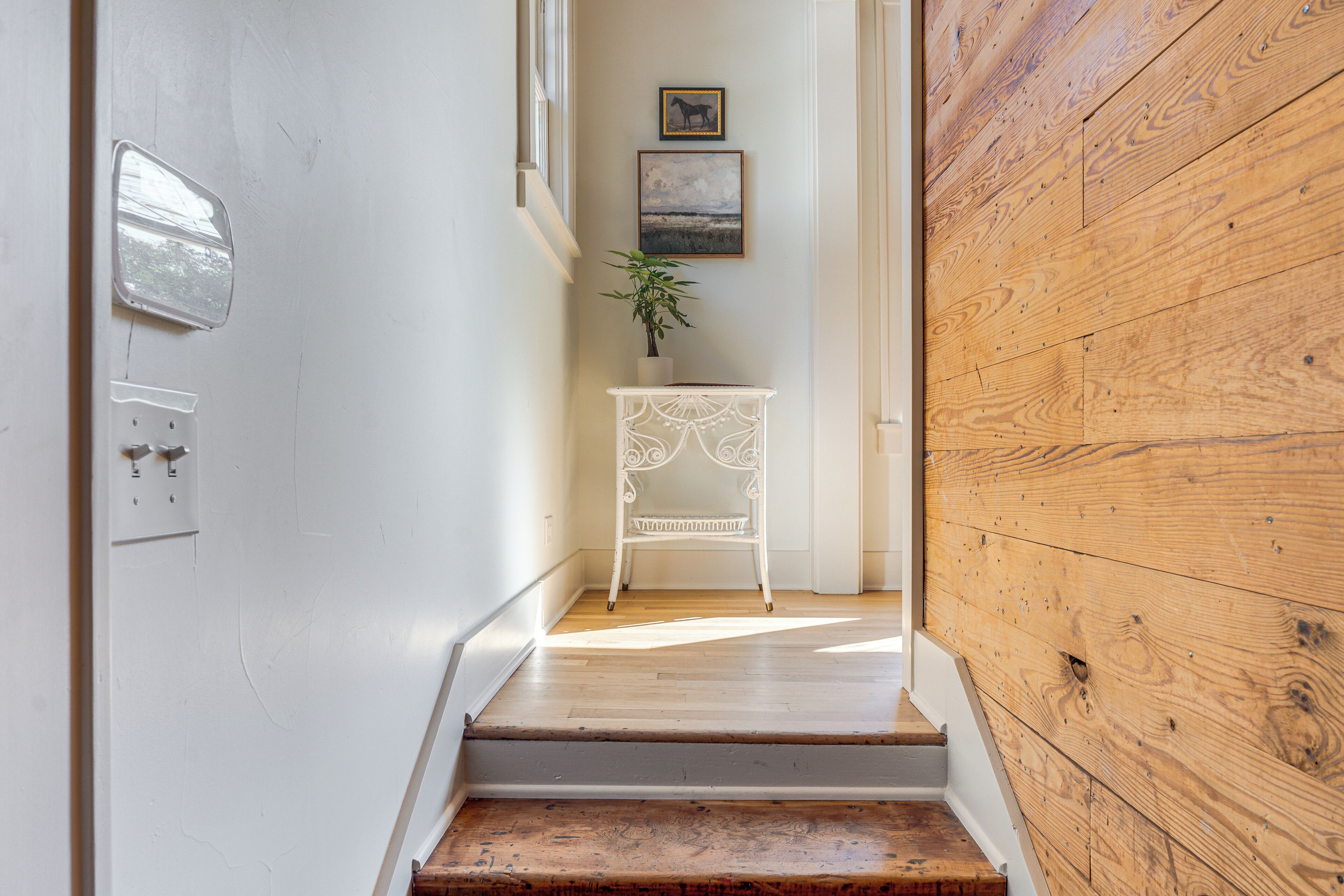 Un escalier en bois mène à un mur blanc où se trouve une petite table et une plante.