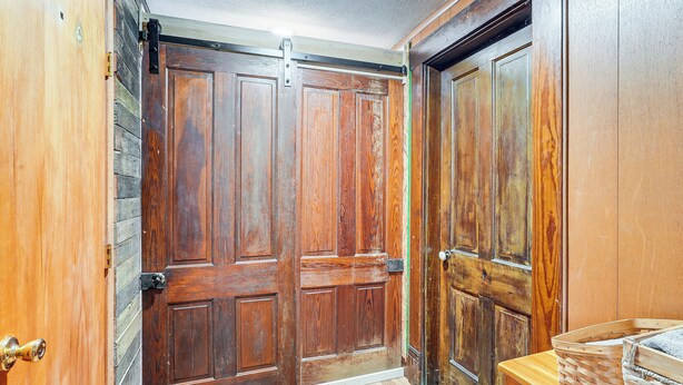 Een houten deur met een verschuifmechanisme, een houten wand en een houten bankje met manden.