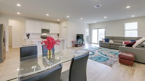 A modern living space with a glass dining table, a grey sofa, and a kitchen area with white cabinets and a microwave. - Buda Business-Ready House: Office, Home Gym & Yard (Buda)
