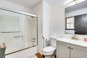 Ein Badezimmer mit Duschkabine aus Glas, Toilette, Waschbecken mit Spiegel und einer Handseifenflasche auf der Ablagefläche.