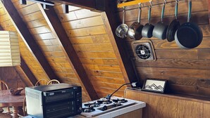 A kitchen with a stove, microwave, and wooden cabinets. - Mid-Century 1960s A-Frame Cabin – Mountain Views - 5 mi to Snow Valley (Running Springs)