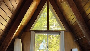 A bedroom with a large bed, a window, and a lamp. - Mid-Century 1960s A-Frame Cabin – Mountain Views - 5 mi to Snow Valley (Running Springs)