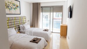 A hotel room with two beds, a large window with a view, a painting on the wall, and a wooden side table. - Premium central duplex 120m2 + Garage and high-speed WiFi (Dar-el-Beida)