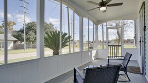 A covered porch with a ceiling fan, large windows, and outdoor seating. - Cajun Country Getaway! Historic Lutcher Bungalow (Lutcher)
