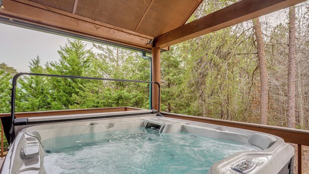 Un jacuzzi con terraza de madera y vistas a un bosque.